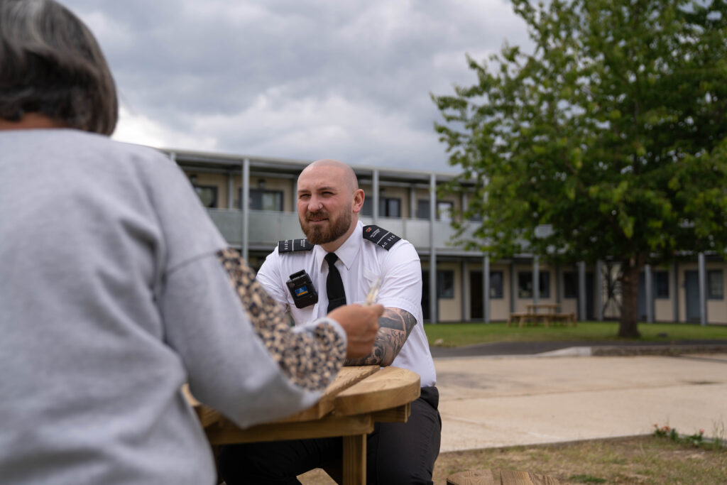 HMP Send male officer talking to a prisoner in the prison grounds